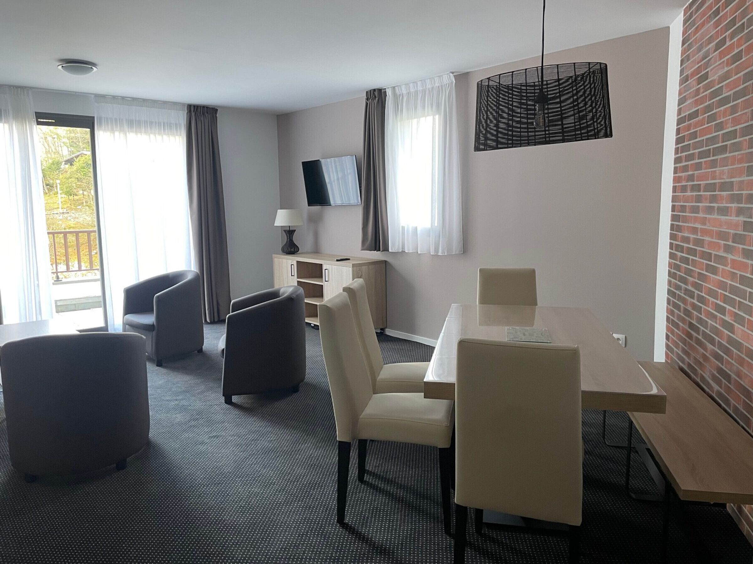 A modern hotel room with a dining area, a TV mounted on the wall, and a view of the outdoors.