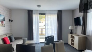 A modern hotel room with a sofa, armchairs, a small table, a TV, and a balcony with curtains. - Studio cabin in Gourette, 6 people, pool, pets allowed (Gourette)