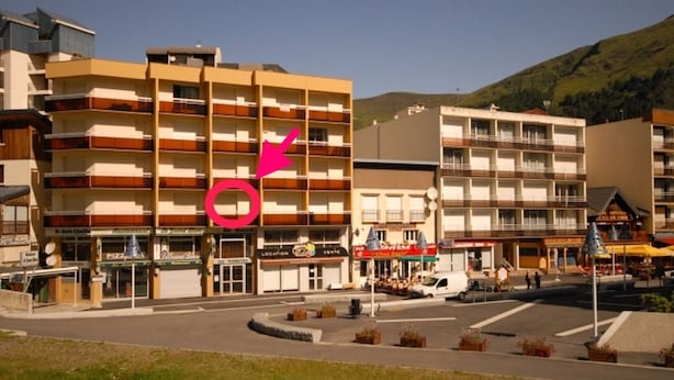 Et hotel med flere etager, en central gårdsplads, udendørs siddepladser og et bjerg i baggrunden.
