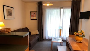 En stue med en sofa, et sofabord, et lille bord med en vase og et fjernsyn på væggen.