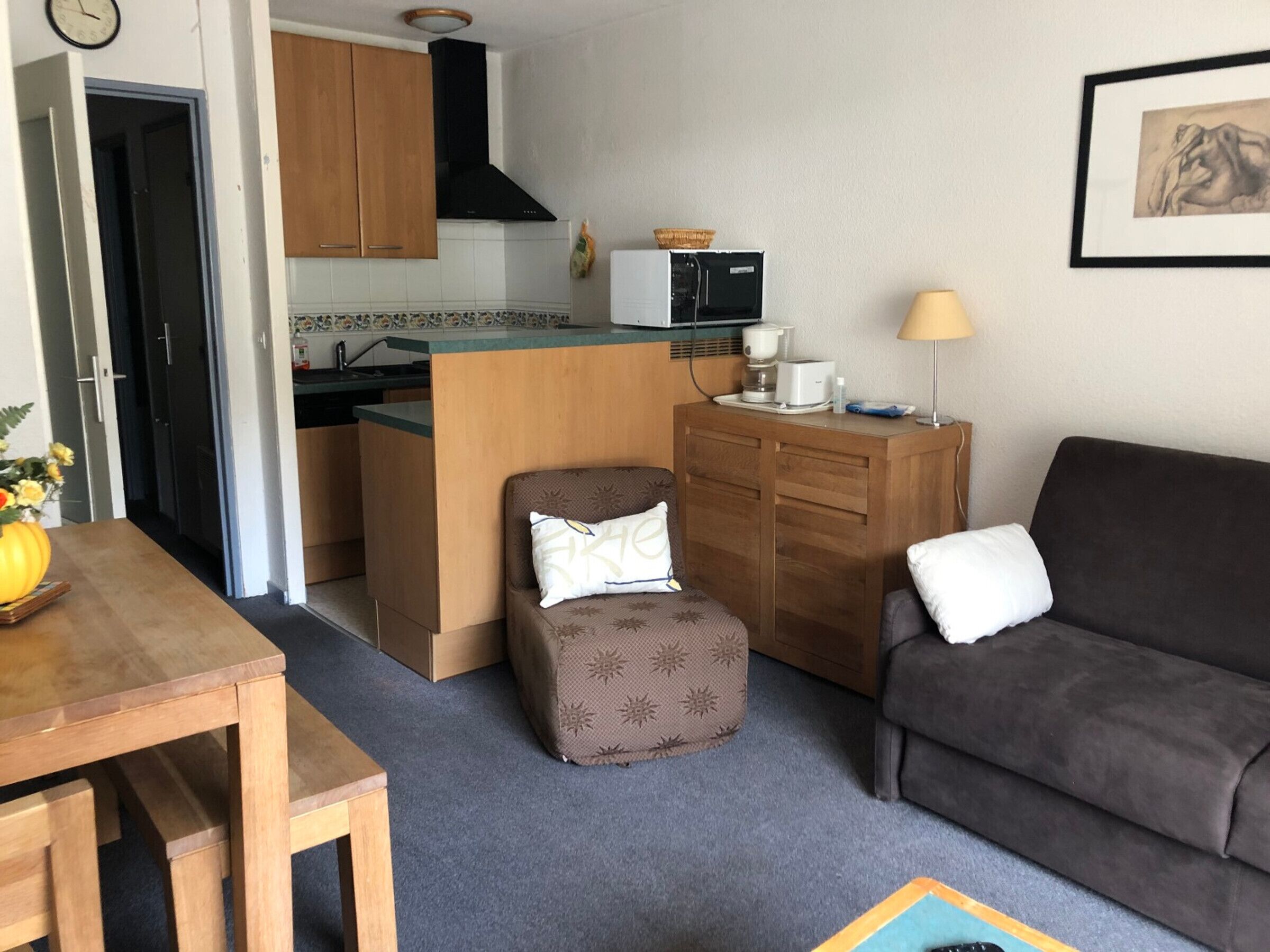 Ein gemütlicher, kompakter Wohnraum mit einer Küchenzeile, einem Esstisch, einer Couch und einem kleinen Hocker.