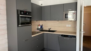 Una cocina compacta con armarios grises, un horno negro, un microondas y una encimera de madera.