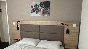 A neatly made bed with a white duvet, a wooden headboard with integrated lighting, and a wall-mounted picture. - Gourette: 2-Room Apt, 6 People, Pool, Pets Allowed (Gourette)
