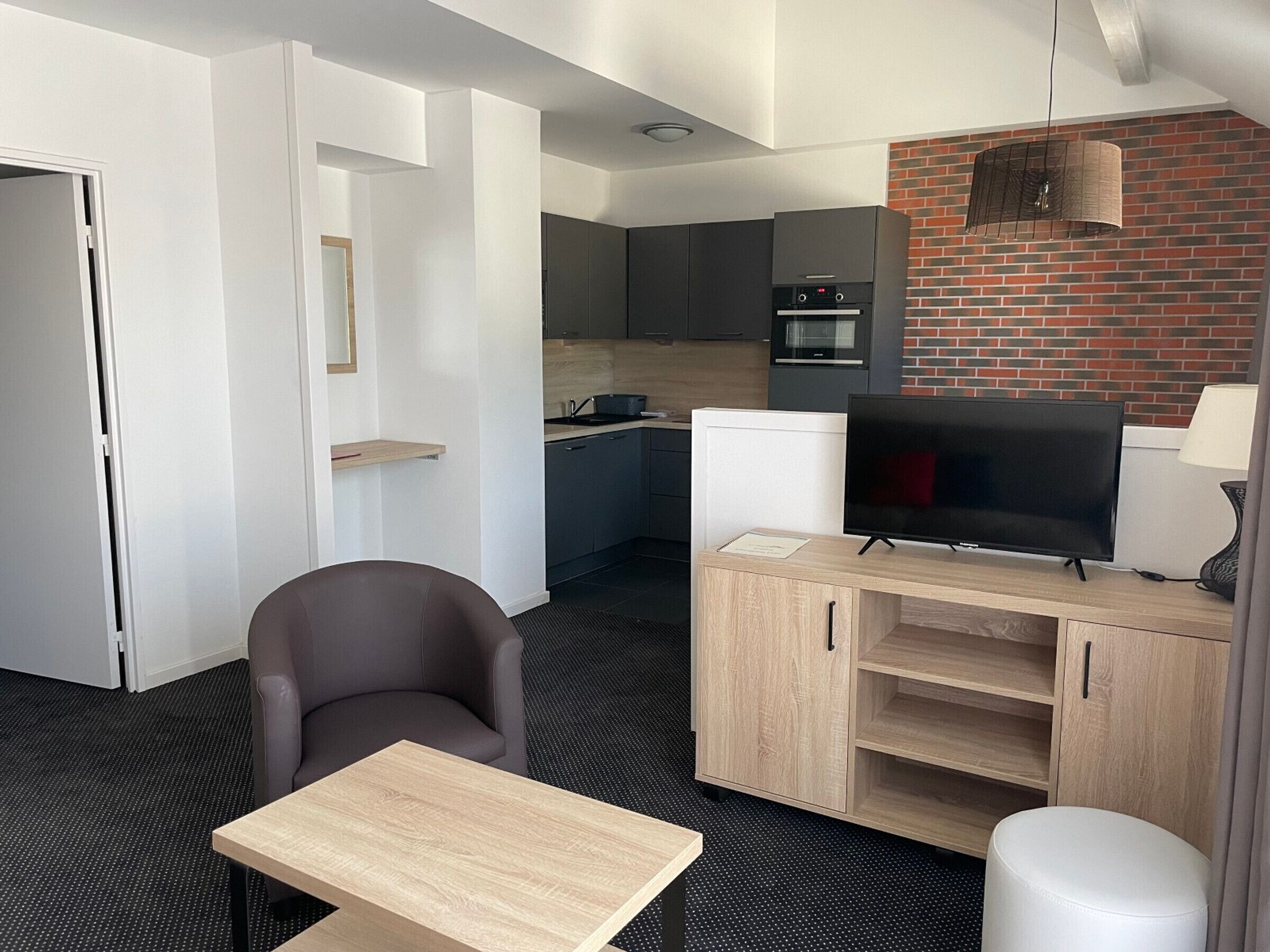 A modern hotel room with a dining area, kitchenette, and a TV.