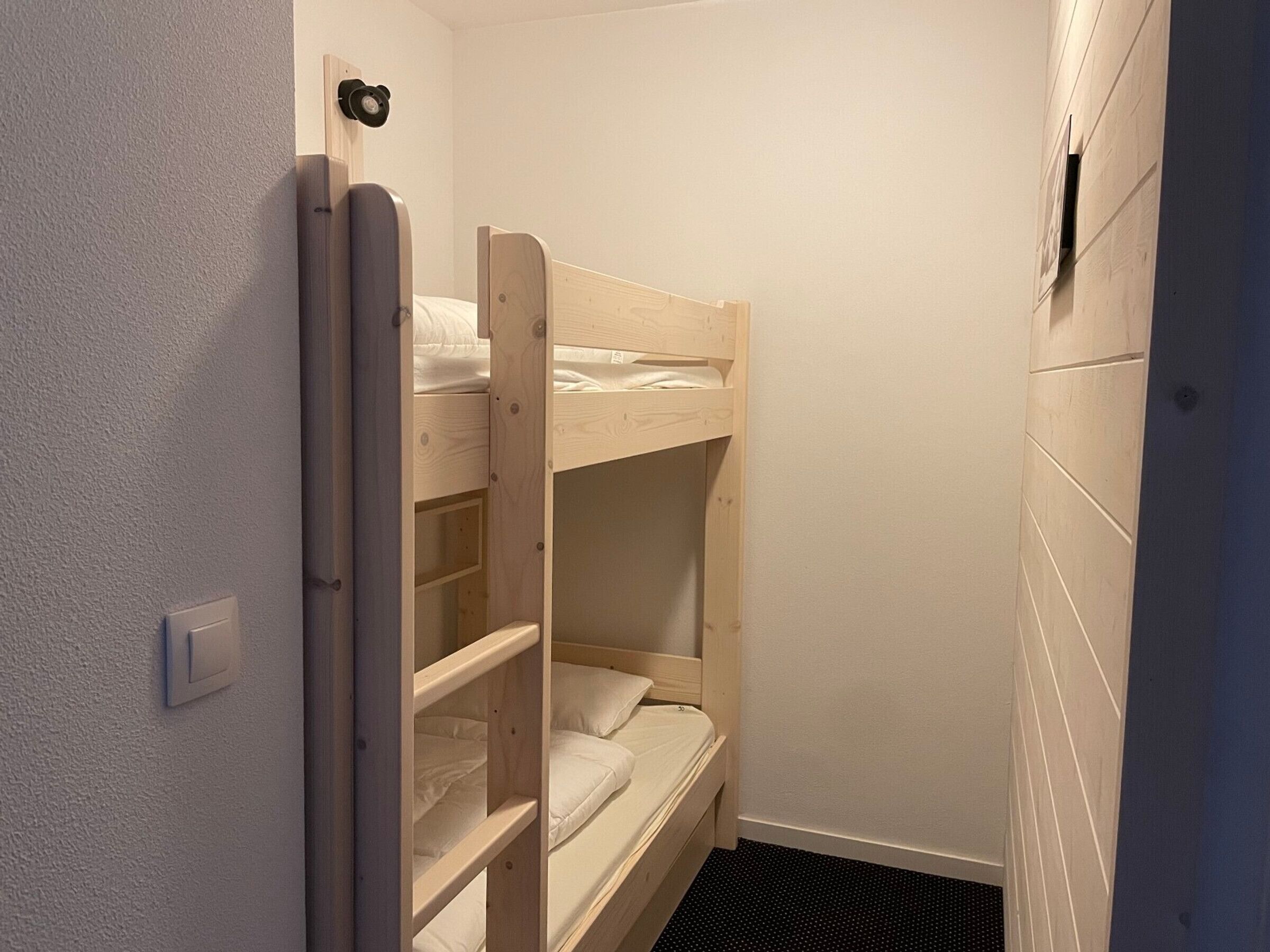 Een kleine, smalle kamer met een stapelbed en een deur.