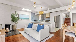 Cozinha moderna com forno embutido, área de refeições com mesa de madeira e sala de estar com sofá branco.