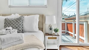 Quarto com cama, mesa de cabeceira, luminária e vista para um deck de madeira através de uma porta de vidro deslizante.