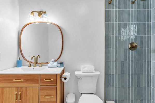 Ein Badezimmer mit rundem Spiegel, zwei Waschbecken, Toilette und Duschbereich.