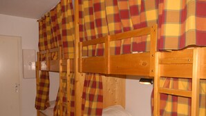 Une chambre avec un lit superposé, des rideaux à carreaux et une tête de lit en bois.