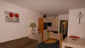 Un espace de vie compact comprenant un canapé, une table à manger avec des chaises, un coin cuisine et une horloge murale.