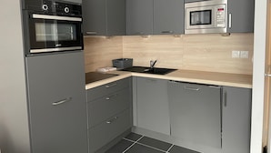 Uma cozinha compacta com armários cinza, um forno preto, micro-ondas e bancada de madeira.