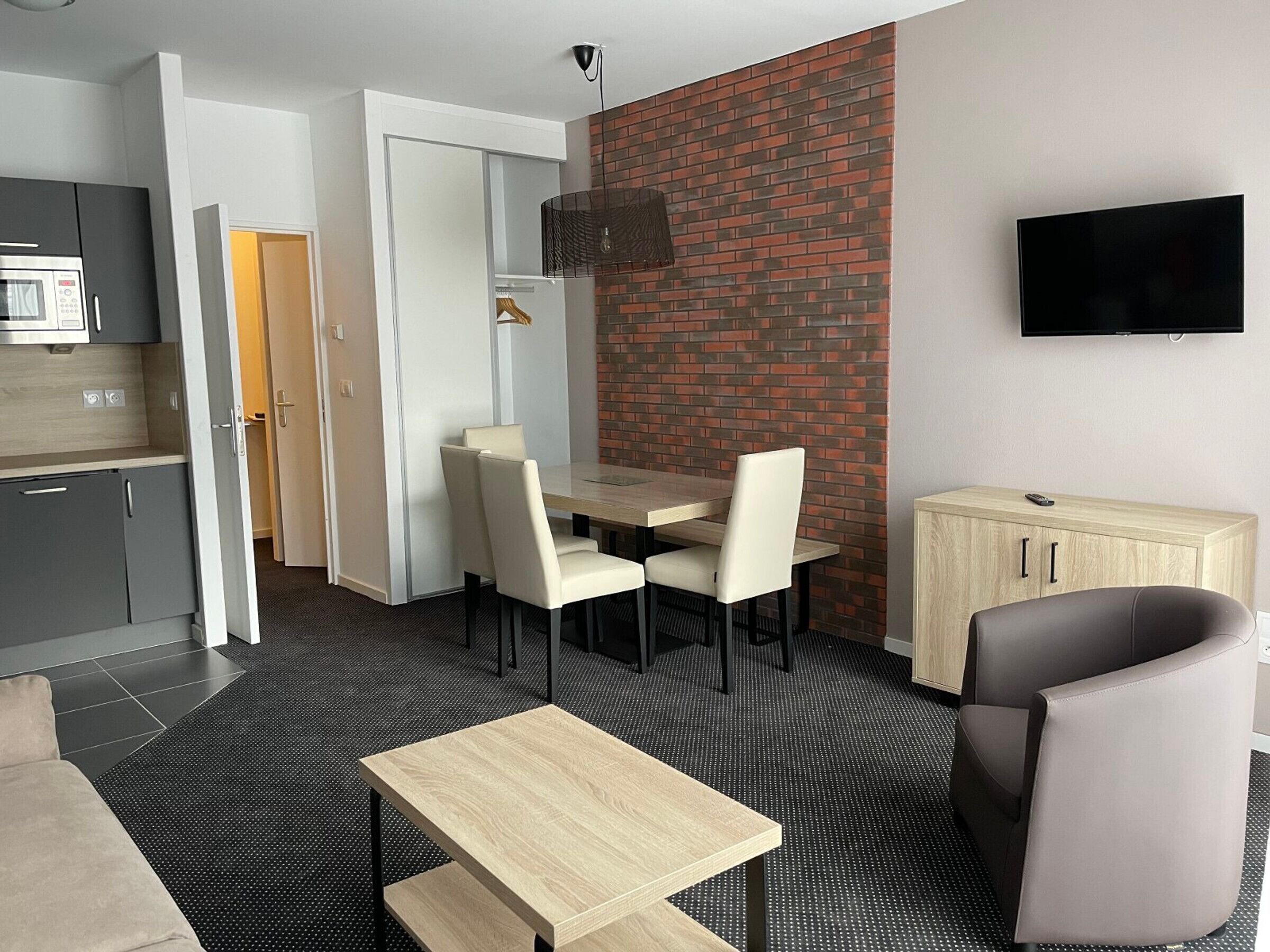 Una habitación de hotel moderna con zona de comedor, televisor montado en la pared y espacio para la cocina con microondas.
