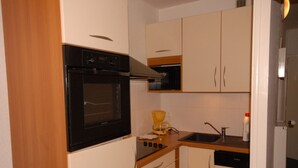 A compact kitchen with white cabinets, a black oven, a coffee maker, and a dishwasher. - Comfort studio 6 pers, Gourette resort, pets allowed (Gourette)