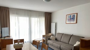 Quarto de hotel com área de refeições, sofá, televisão e um quadro na parede.