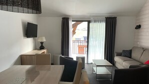 Una habitación de hotel moderna con un escritorio de madera, un sofá, una mesita y un televisor montado en la pared.