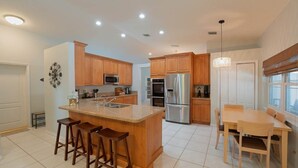 A modern kitchen with wooden cabinets, stainless steel appliances, a central island with stools, and a dining area with a table and chairs. - ‼️Poolside Miami Paradise w/ BBQ + Outdoor Lounge (Miami)