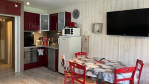 Kompakti keittiö, jossa on punaiset kaapit, mikroaaltouuni, jääkaappi ja ruokapöytä punaisine tuoleineen.