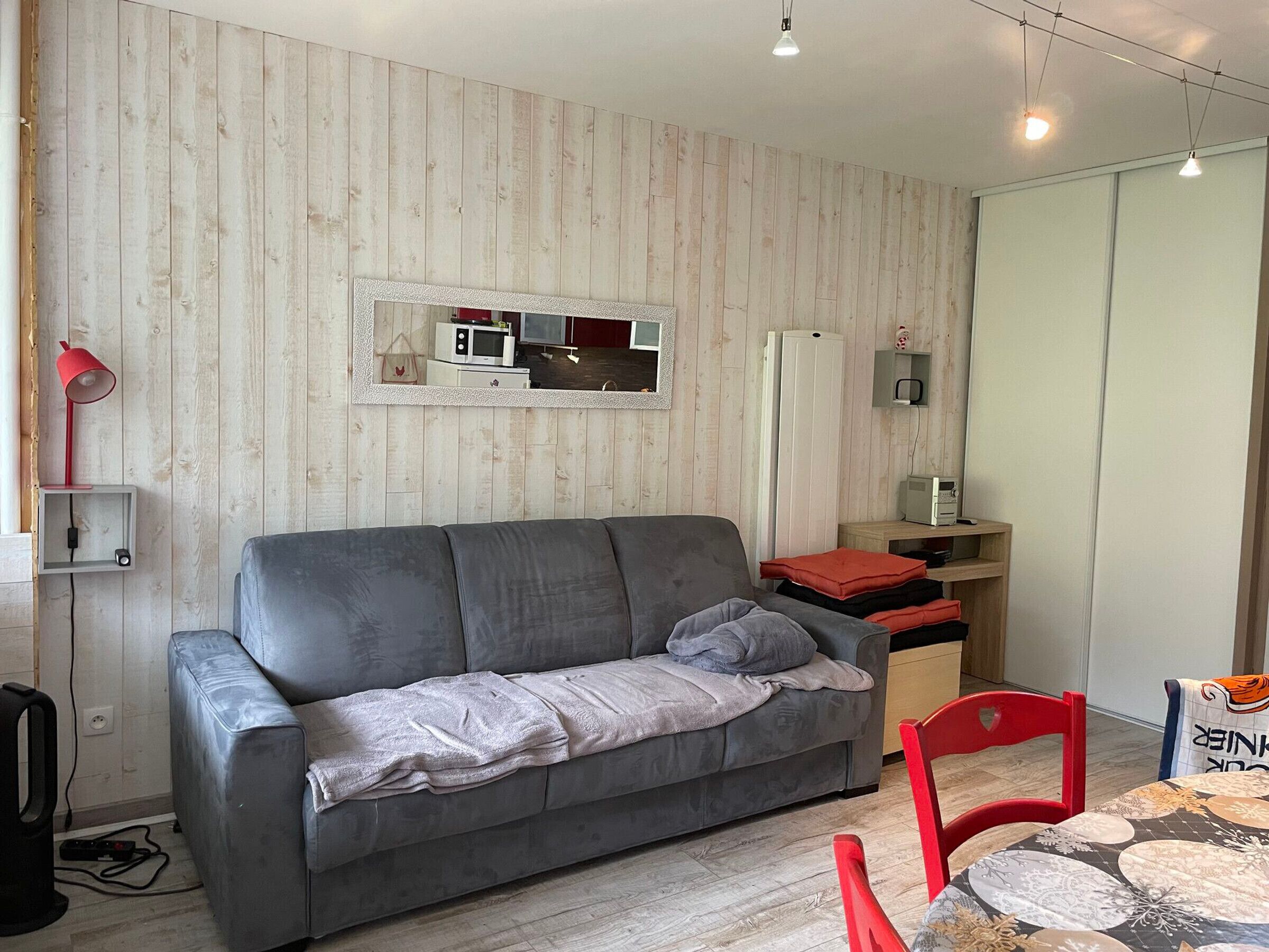 Ein modernes Wohnzimmer mit einem grauen Sofa, einem roten Sessel und einem kleinen Tisch mit einem gemusterten Tischläufer.
