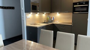 Een moderne keuken met een magnetron, oven en een spoelbak. Er staan stoelen rond een tafel.