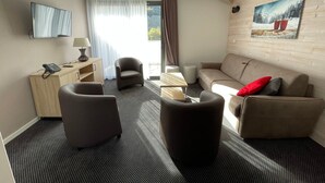 Een moderne hotelkamer met een bank, fauteuils, een bureau met telefoon, een lamp en een schilderij aan de muur.