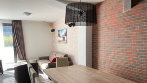Een moderne kamer met een houten eettafel, beige stoelen, een bank en een bakstenen muur.