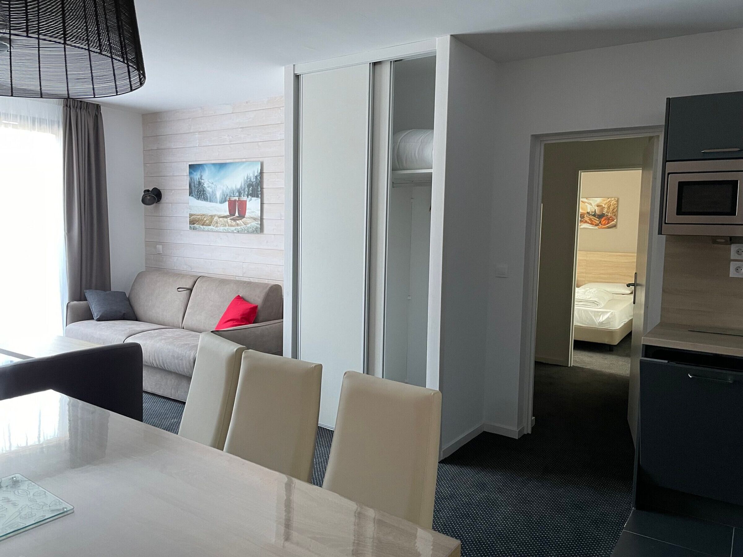 A hotel room with a sofa, a dining table, a kitchen area, and a sliding door leading to a bedroom.