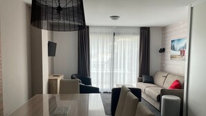 Ein modernes Hotelzimmer mit Esstisch, Stühlen, einer Couch und einem großen Fenster mit Vorhängen.