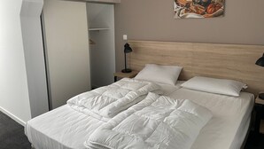 Ein ordentlich bezogenes Bett mit weißen Leinentüchern, einem hölzernen Kopfteil und einem kleinen Nachttisch mit Lampe.