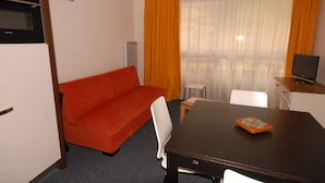 Ein gemütliches Hotelzimmer mit einer Sitzecke, einem kleinen Tisch, einem Fernseher und einem Fenster mit Vorhängen.