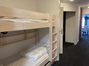 Habitación con literas de madera, una cama individual y una puerta que da a un pasillo.