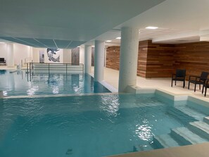 Una piscina interior con agua cristalina, una pared de madera y un área de descanso con sillas.