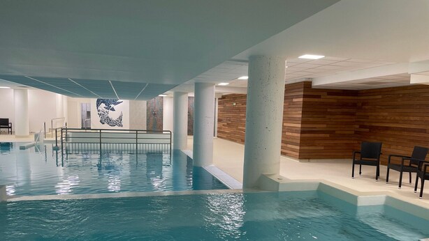 Una piscina interior con agua cristalina, una pared de madera y un área de descanso con sillas.