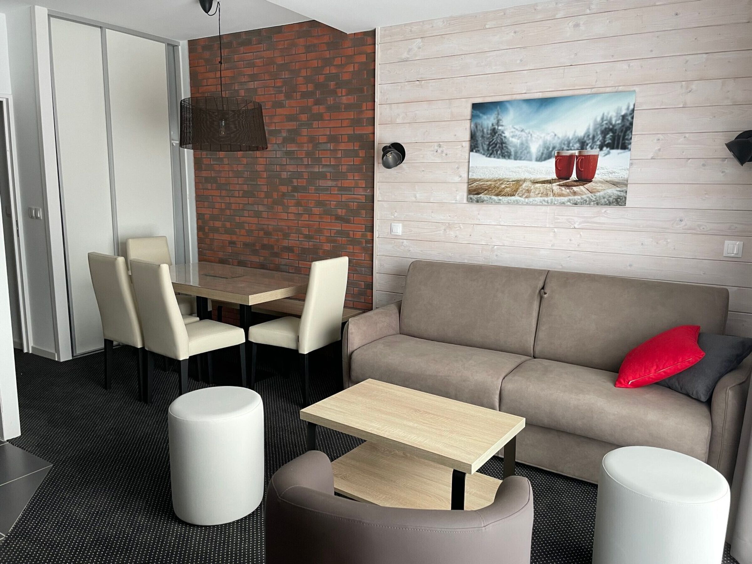 A modern living room with a sofa, two chairs, a coffee table, and a TV mounted on a brick wall.