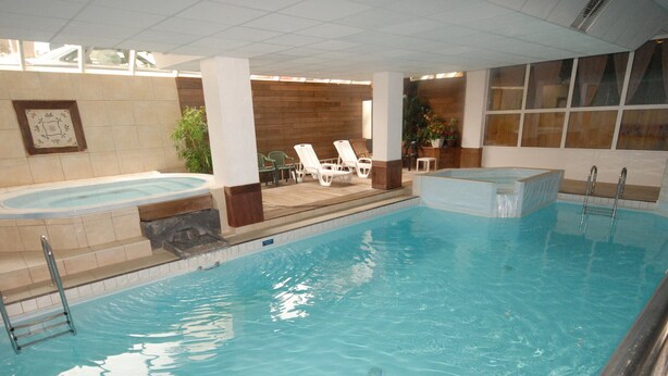 Una piscina interior con jacuzzi, sillas de descanso y pared de azulejos.