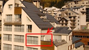 Un edificio de varios pisos con balcones, un coche estacionado adelante y una flecha roja señalando una ventana.
