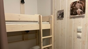 A bunk bed with a ladder, a lower bunk with a pillow, and a wall-mounted light switch.