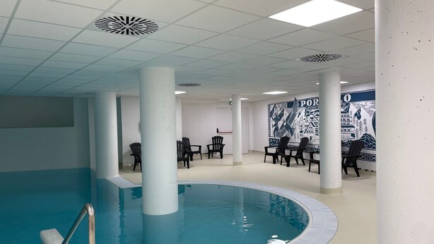 Una piscina interior con suelo de baldosas, sillas reclinables negras y un mural en la pared.