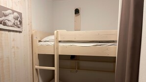 Una cama litera con escalera de madera y un estante, un pequeño estante con un cuadro, y un gancho fijado a la pared.