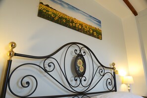 Un lit avec une tête de lit en métal noir, un tableau de tournesols et une lampe sur la table de chevet.
