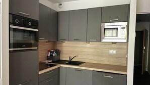 A compact kitchen with grey cabinets, a built-in oven, a microwave, and a sink. - Gourette studio pool 4 pers., pets allowed (Gourette)