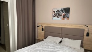 En pænt redt seng med hvide sengetøj, et træsengegærde og et natbord med en lampe.