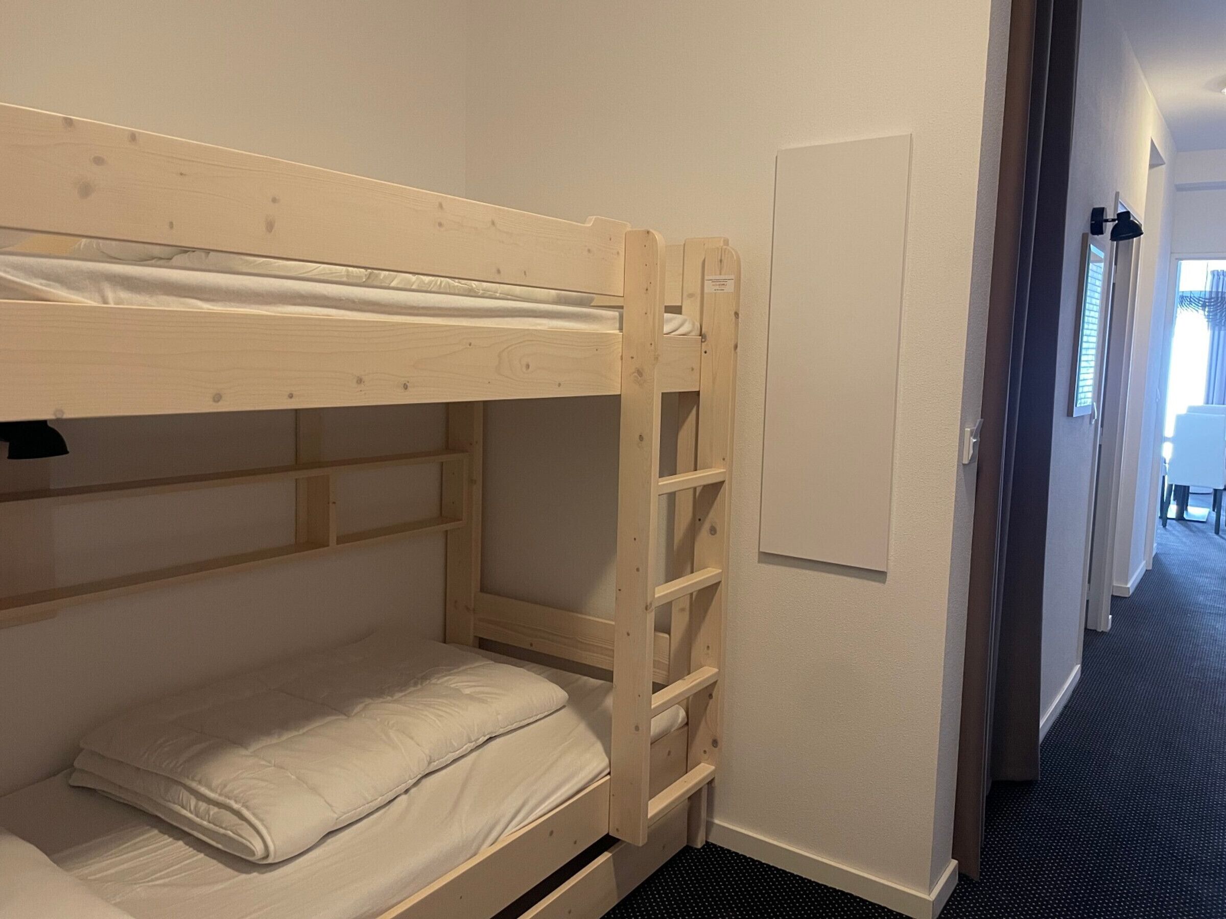 A bunk bed with a ladder, a small shelf, and a door in a hotel room.