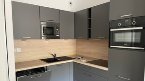 Een compacte keuken met grijze kastjes, een inbouwoven, een magnetron en een vaatwasser.