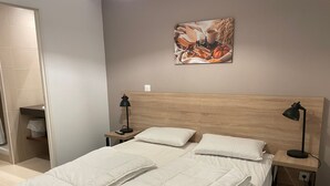 Een netjes opgemaakt bed met witte beddengoed, een houten hoofdbord en twee nachtkastjes met lampen.