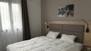 Ein Hotelzimmer mit einem großen Bett, einem Kopfteil mit wandmontierten Leselampen, einem Bild an der Wand und einem Fenster mit Vorhängen.