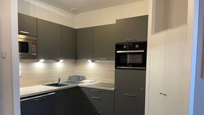 Eine kleine Küche mit dunklen Schränken, einer Mikrowelle, einem Backofen und einem Spülbecken.