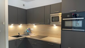 Eine moderne Küche mit dunklen Schränken, einem Edelstahlbackofen und einer Mikrowelle.