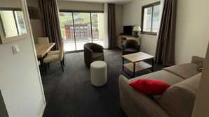 Ein Hotelzimmer mit Balkon, einer Couch, einem Sessel, einem kleinen Tisch und einem Fernseher.