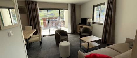 A hotel room with a balcony, a sofa, a chair, a small table, and a TV.