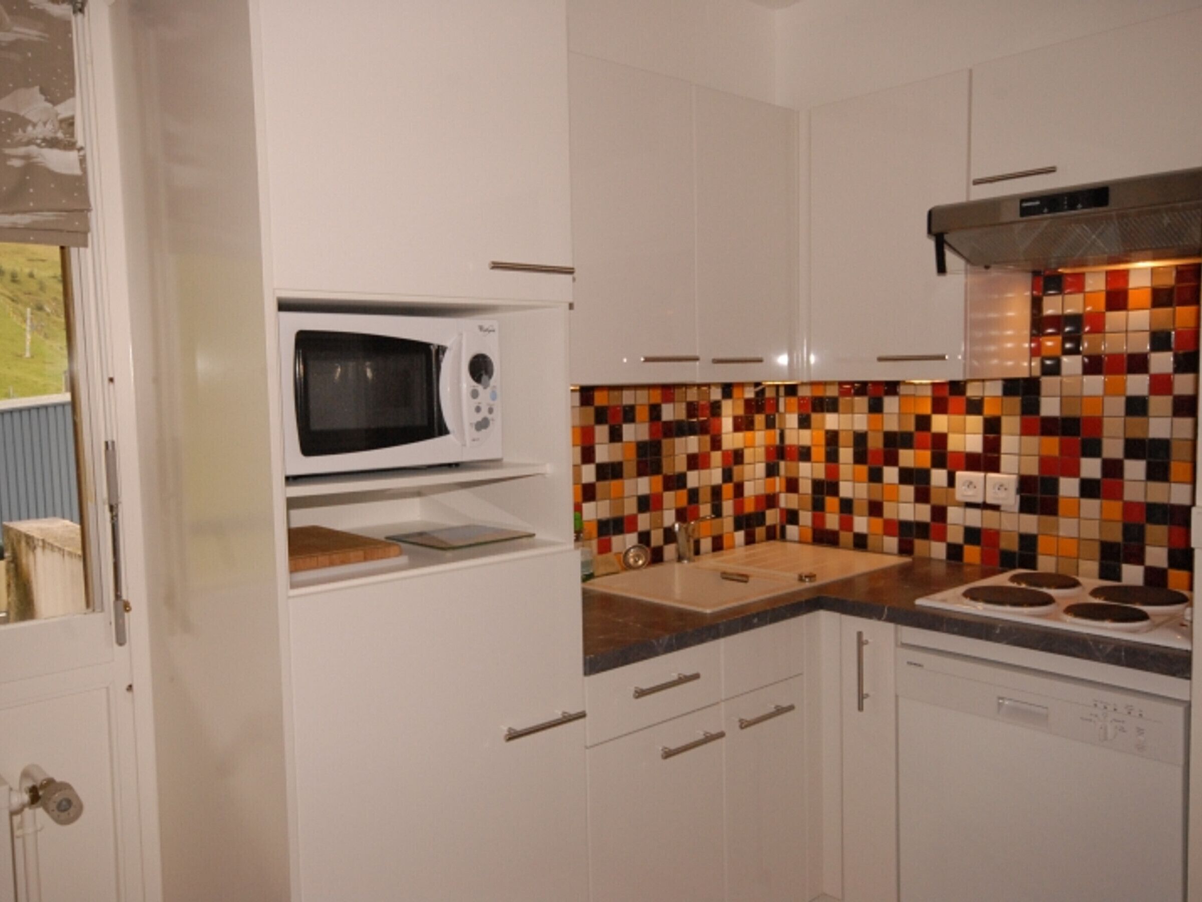 A kitchen with white cabinets, a microwave, a stove, and a colorful mosaic backsplash.